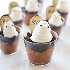 A dessert cup filled with pudding, a cookie headstone, and a whipped cream ghost.