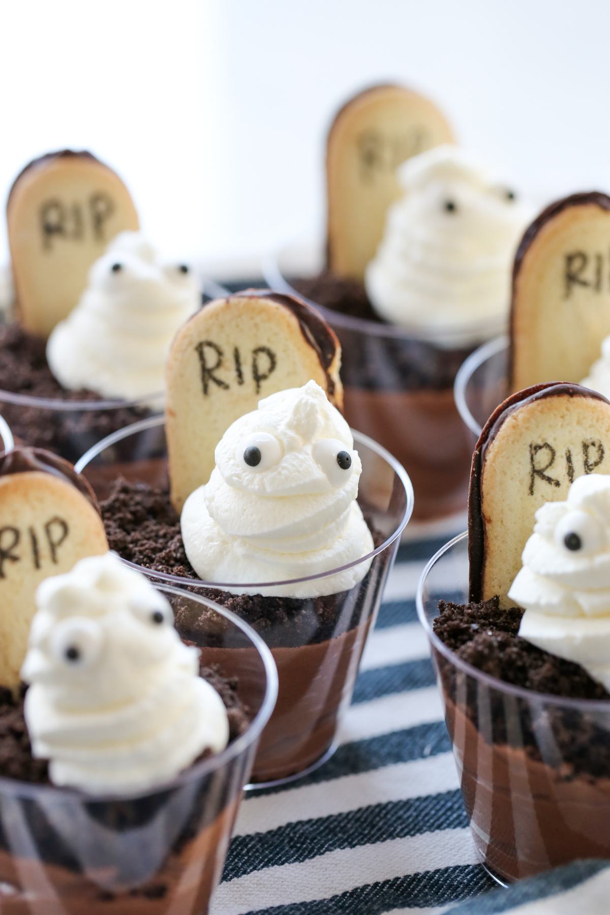 A dessert cup filled with pudding, a cookie headstone, and a whipped cream ghost. 