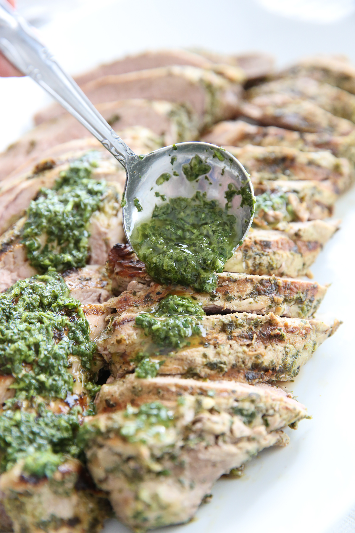 spooning chimichurri sauce over pork tenderloin
