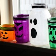 Halloween mason jar lanterns made to look like a pumpkin, ghost, Frankenstein's monster, etc. on a window sil.