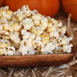 A plate full of stove top kettle corn on a bed of straw, with pumpkins in the background.