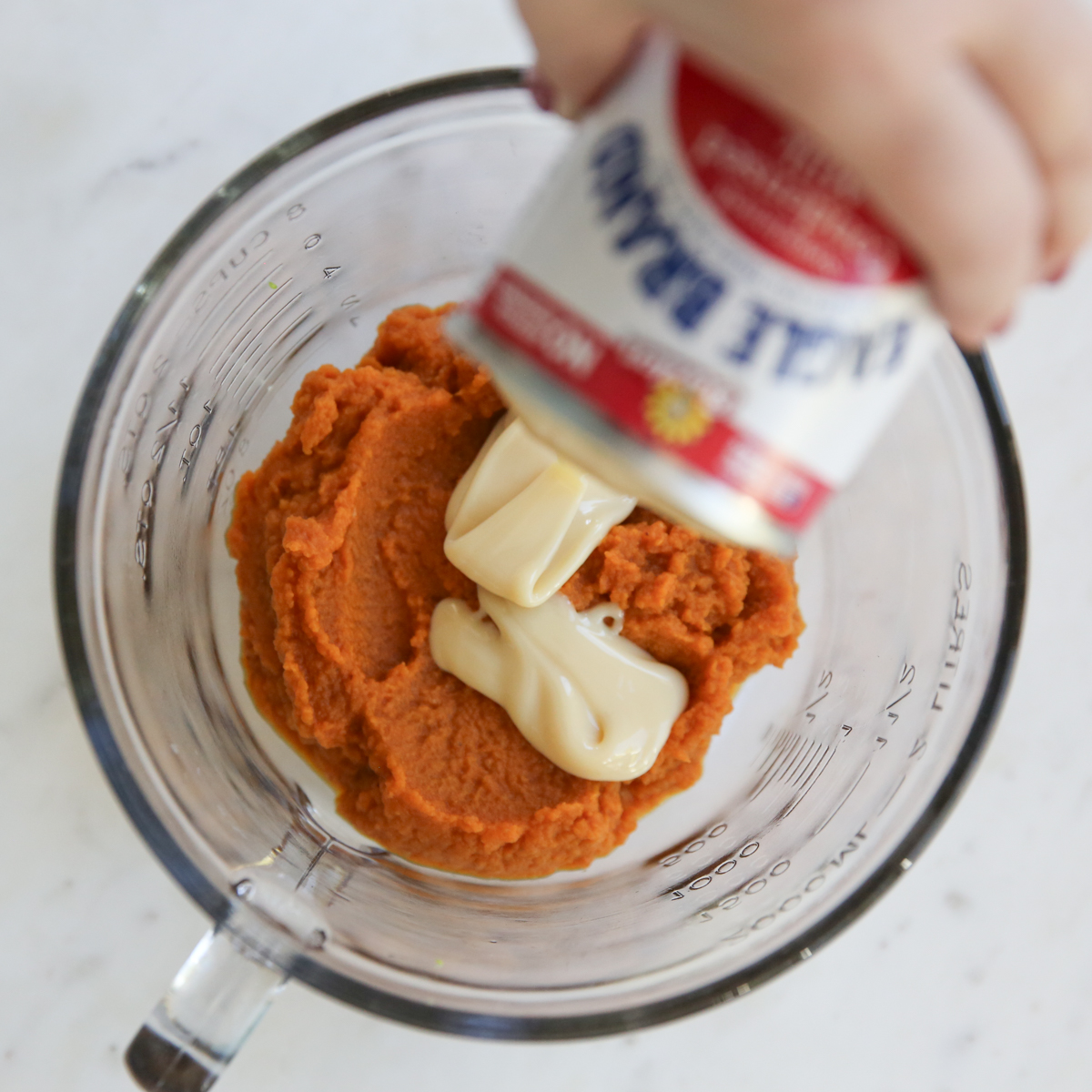 pouring sweetened condensed milk over pumpkin puree
