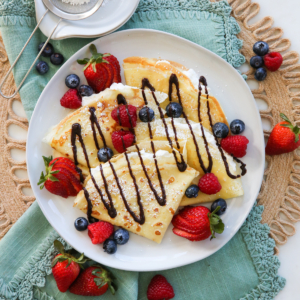 A plate of crepes with berries and chocolate drizzle.