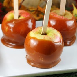 Three apples, dipped in honey caramel, on a white serving tray.