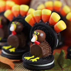 Thanksgiving turkeys made from Oreos, peanut butter cups, whoppers, candy corn, and frosting, lined up in a row.