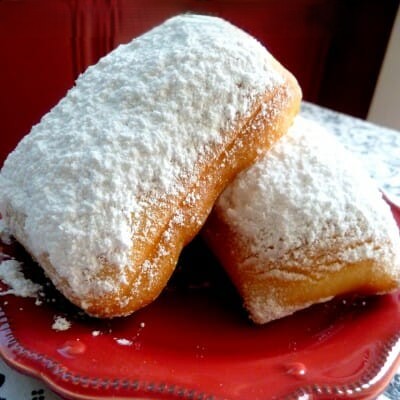 Two beignets dusted with powdered sugar on a red plate.