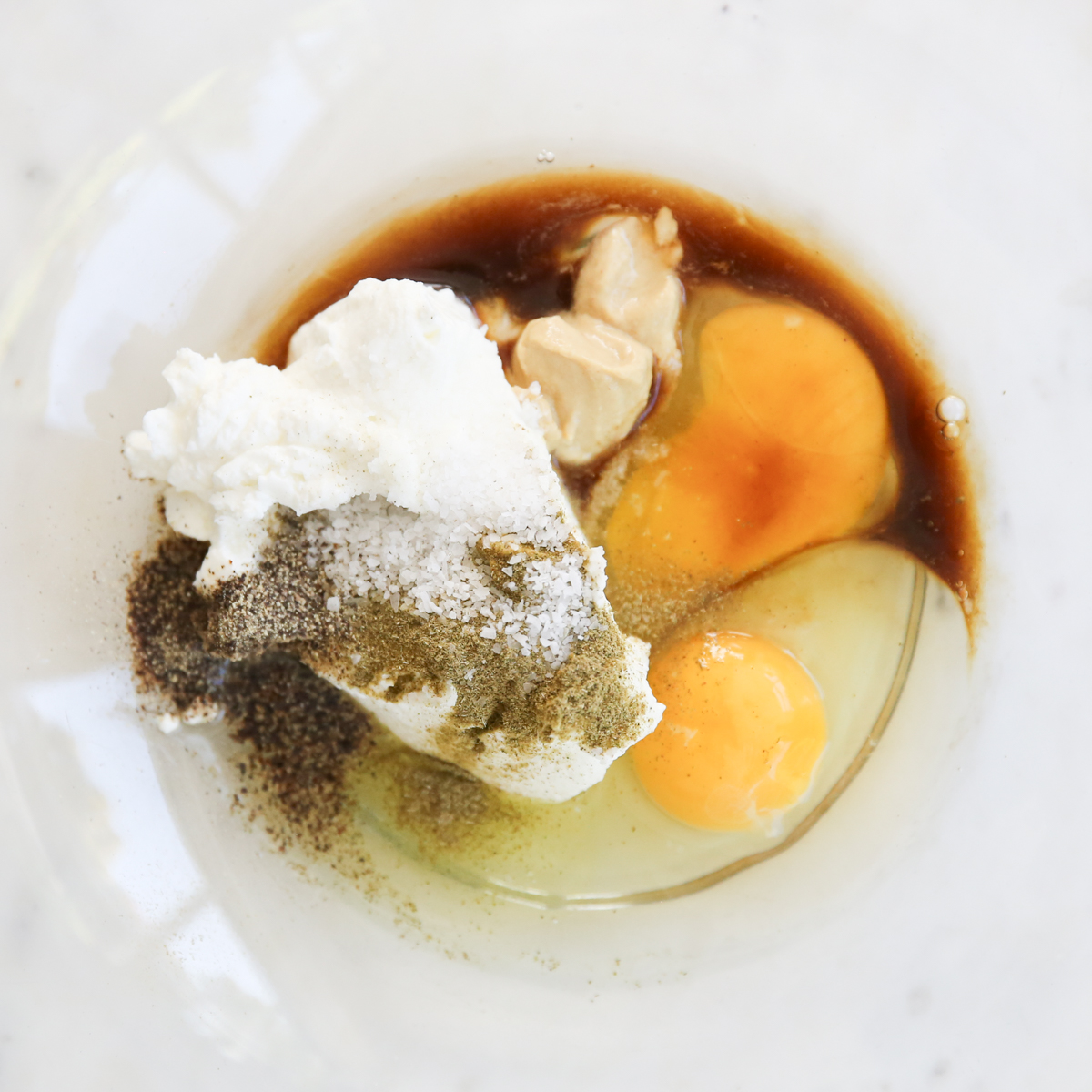 eggs, yogurt, chili sauce, and other meatloaf ingredients in a glass bowl