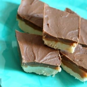 Peanut Butter Cup Shortbread Bars stacked on a teal plate. Each bar has a bottom shortbread layer, then a caramel peanut butter layer, and a chocolate top layer.