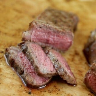 Slices of perfectly cooked steak on a wood cutting board.