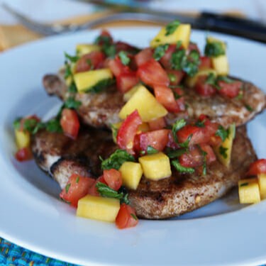 Grilled pork chops on a white plate, covered in mango salsa.