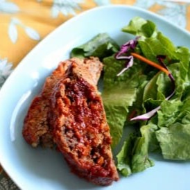 Two slices of meatloaf on a plate with green salad.