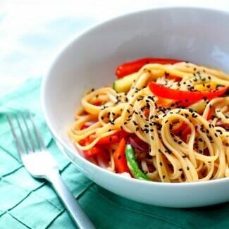 A white b owl filled with stir fried noodles and veggies, topped with black sesame seeds.