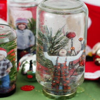 A few homemade snow globes on a table. The snow globes are made from old jars, laminated pictures, and plastic greenery.