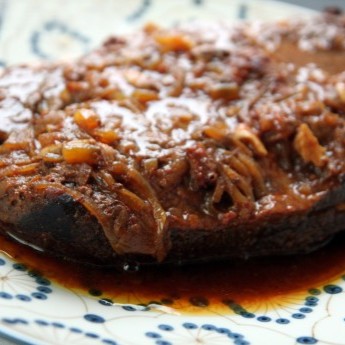 Sweet and tangy brisket, covered in caramelized onions, on a serving dish.