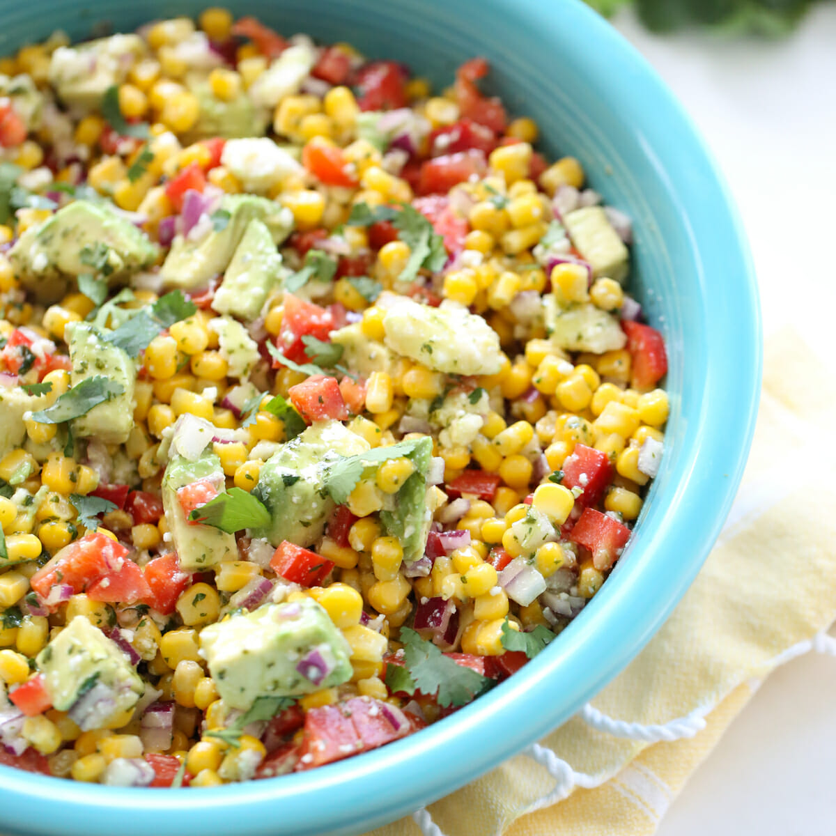 Fresh corn, avocados, and vegetables in a blue bowl