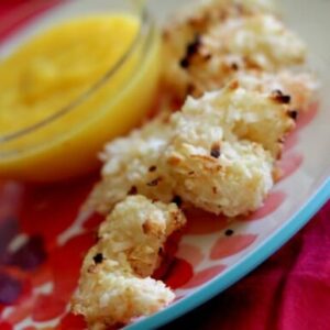 A closeup of crispy coconut macadamia crusted shrimp next to a bowl of yellow dipping sauce.