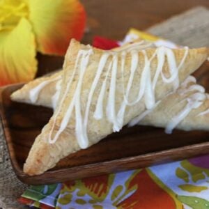Two coconut turnovers on a serving plate with a drizzle of glaze.