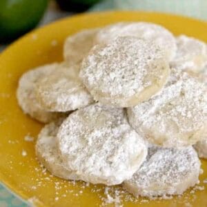 A pile of little lime meltaway cookies, coated in powdered sugar, on a yellow plate.