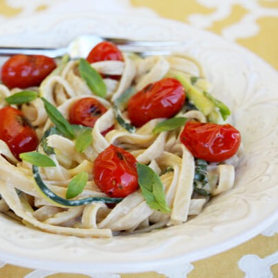 A white bowl filled with pasta, zucchini noodles, and grape tomatoes.