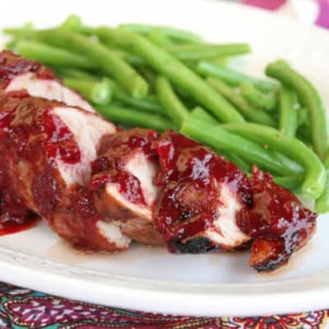 Slices of pork tenderloin with deep red plum sauce spooned over the top, alongside a serving of green beans.
