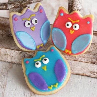 Cute sugar cookies decorated to look like owls with colored frosting and candy eyes, using a tulip shaped cookie cutter.