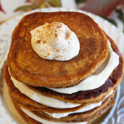 A stack of pumpkin pancakes with cream layered between.