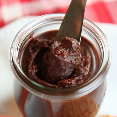 A knife dipping into a little glass pot of chocoalte hazelnut spread.