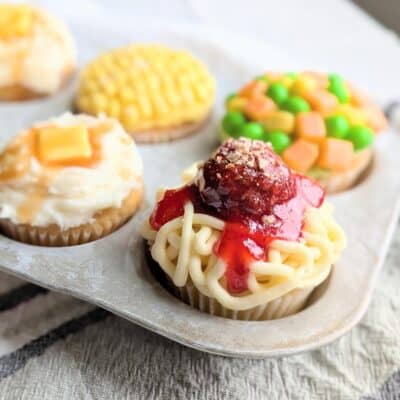 A funny cupcake with frosting squiggles and a candy meatball in strawberry sauce that looks like spaghetti and meatballs.