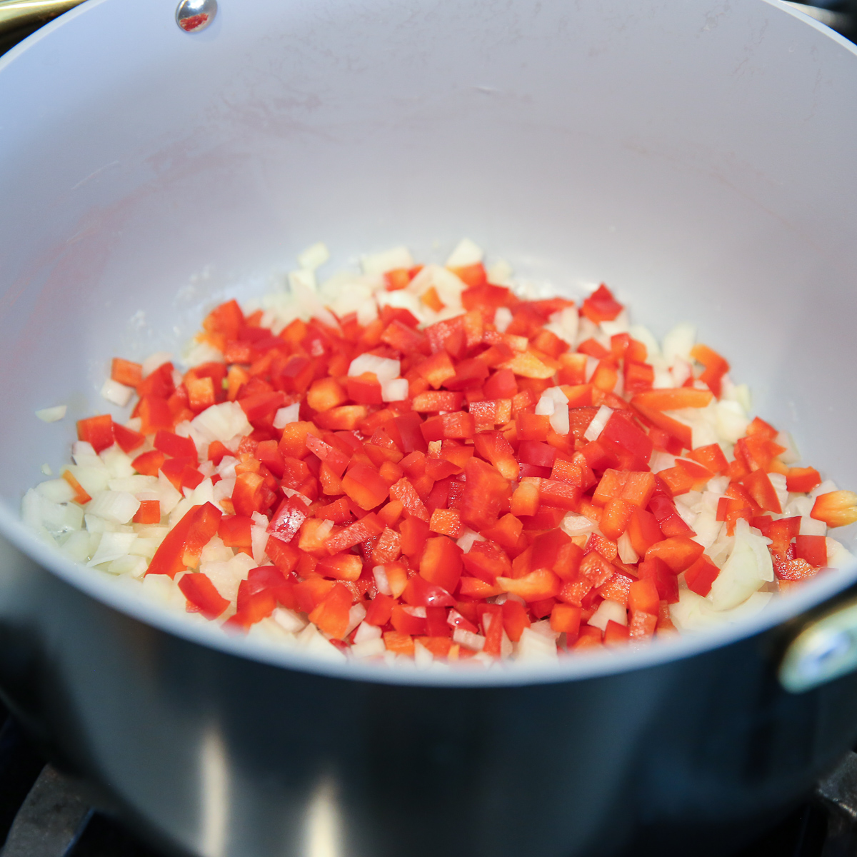 diced red bell peppers and onions in a pot being sauteed