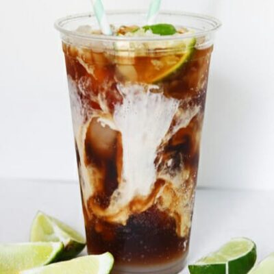 A closeup of a glass of diet coke, ice, limes, and a dash of cream.