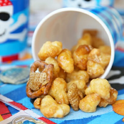 Caramel covered pirate's booty snack mix spilling out of a cup onto a colorful napkin.