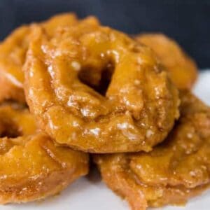 A pile pumpkin spice doughnuts on a plate. The doughnuts have a heart shaped hole in the center.