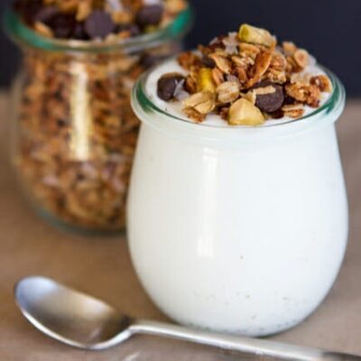 A small glass pot of yogurt topped with homemade granola. Another pot full of just granola sits in the background.