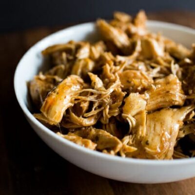 A white bowl filled with shredded taco-seasoned chicken.