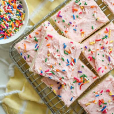 pink frosted sugar cookies stacked on a baking tray
