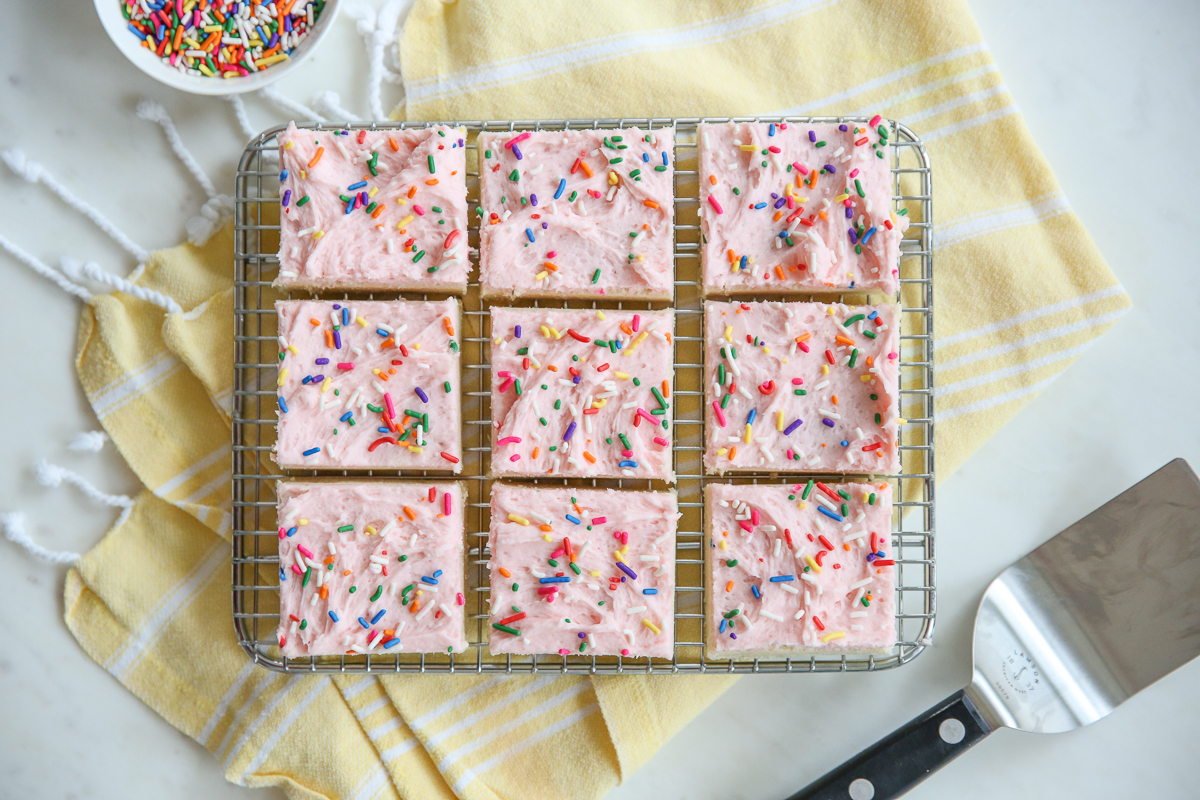 sugar cookie bars with pink frosting on a baking tray