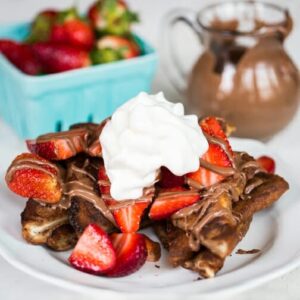 A plate of chocolate French toast, topped with fresh strawberries, chocolate sauce, and whipped cream.