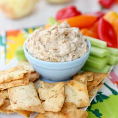 A little blue bowl filled with sweet onion dip, nestled among pita chips and fresh vegetables.