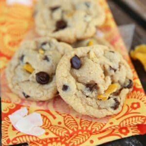 Three dark chocolate chip coconut mango cookies on an orange napkin.