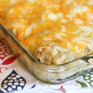 A close up of the corner of a pan of breakfast enchiladas, covered in melty cheese.