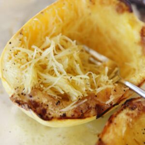 A roasted spaghetti squash half with a fork separating the "spaghetti."