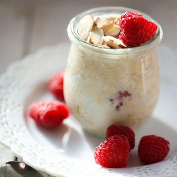 A little glass jar filled with overnight oats, topped with almonds and raspberries.