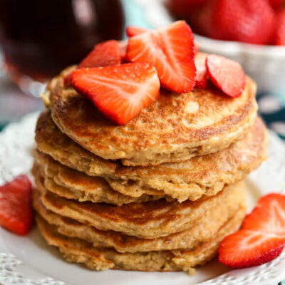 A stack of whole grain oatmeal pancakes, topped with strawberries, on a white plate.