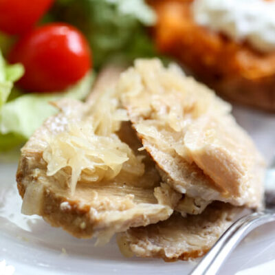A pile of sliced pork on a plate topped with sour kraut, alongside a side salad.