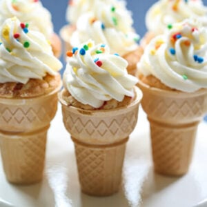 Vanilla cupcakes baked in ice cream cones, topped with a swirl of vanilla frosting and colorful sprinkles.
