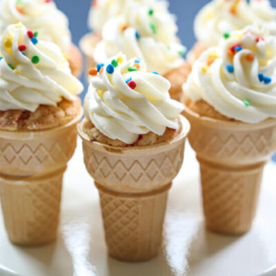 Vanilla cupcakes baked in ice cream cones, topped with a swirl of vanilla frosting and colorful sprinkles.