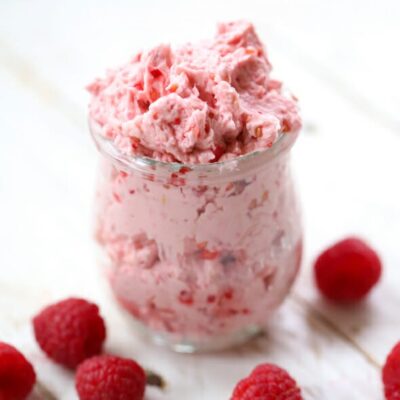 A clear glass jar filled with fluffy, pink raspberry honey butter.