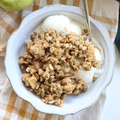bowl of apple crisp and ice cream next to pan full of crisp