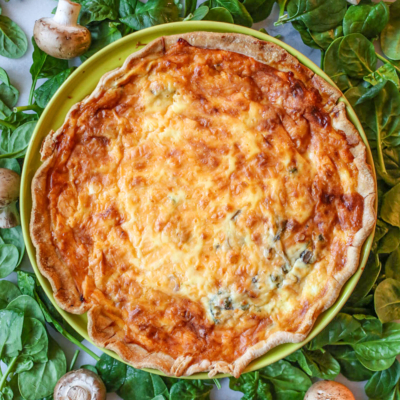 Baked Quiche in a pie plate surrounded by spinach and mushrooms