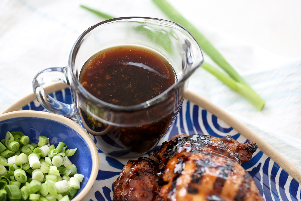 Teriyaki Sauce in a jar with a platter of chicken and bowl of green onions